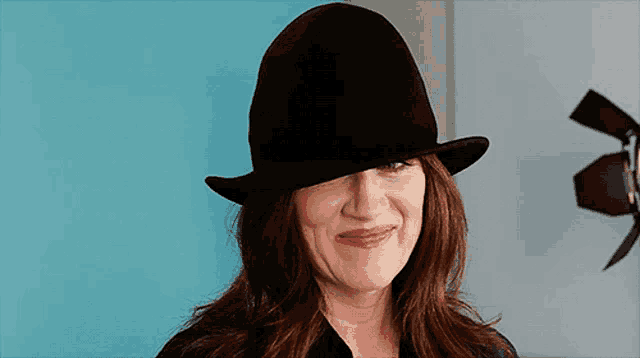 a woman wearing a black hat is smiling in front of a blue wall