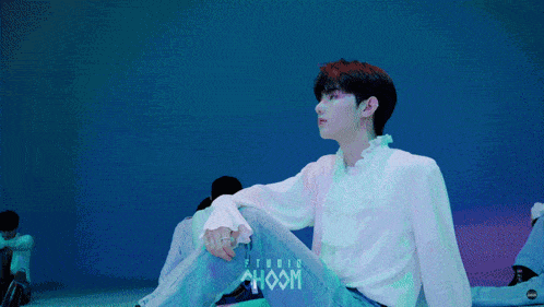 a young man sits in front of a blue wall with the word choom written on it