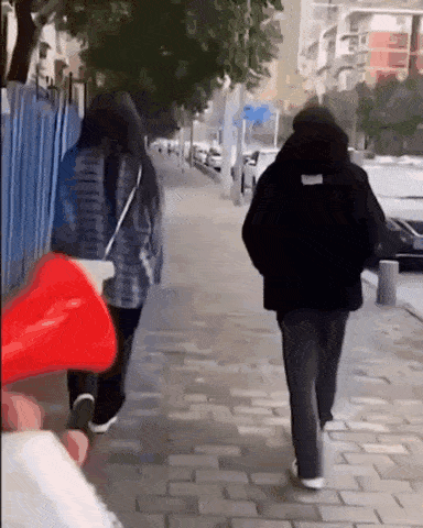 a man and a woman are walking down a sidewalk with a red object in the foreground .