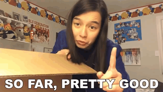 a woman is pointing at a cardboard box with the words so far pretty good below her