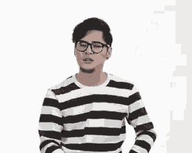 a man wearing glasses and a striped shirt is standing in front of a white wall .