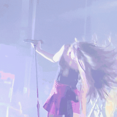 a woman in a pink skirt is holding a microphone in a dark room