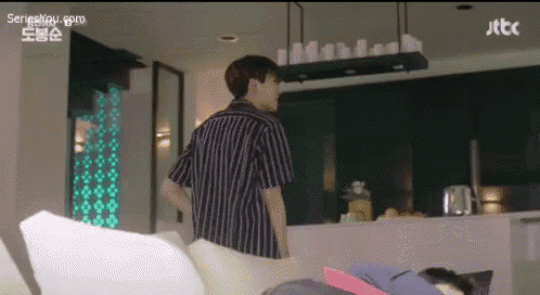 a man in a striped shirt is standing next to a woman laying on a couch in a living room .