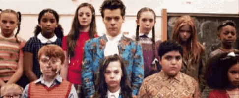 a group of children are posing for a picture with harry styles in a blue suit .