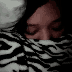 a woman is laying under a zebra print blanket