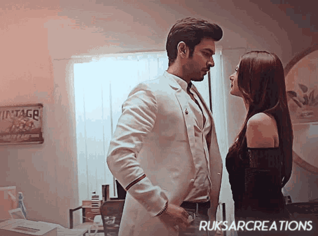 a man in a white suit and a woman in a black dress are looking at each other