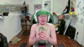 a man wearing headphones and a green hat holds a bunch of money