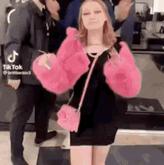 a woman wearing a pink fur coat and a pink purse is dancing .