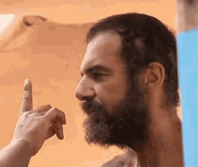 a man with a beard is pointing his finger to his face