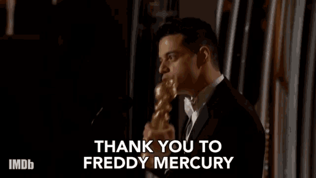 a man in a suit is giving a speech and says thank you to freddy mercury .