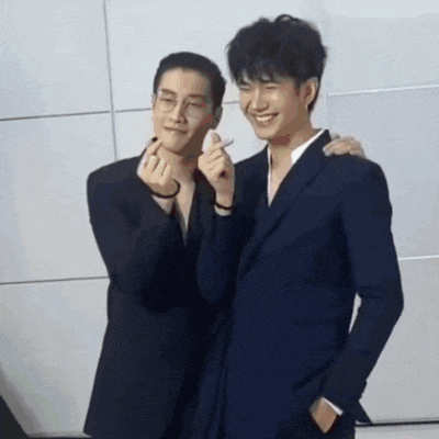 two men in suits and glasses are making a heart shape with their hands