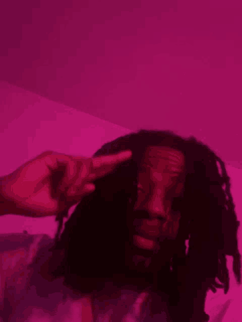 a man with dreadlocks is giving a peace sign in front of a pink background .
