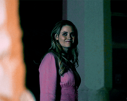 a woman in a pink sweater is smiling in a dark room