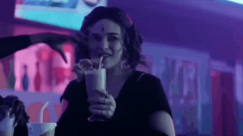 a woman is drinking a milkshake with a straw in a club .