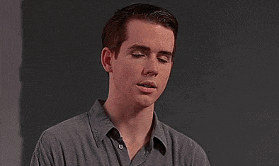 a young man in a grey shirt is standing in front of a black wall .