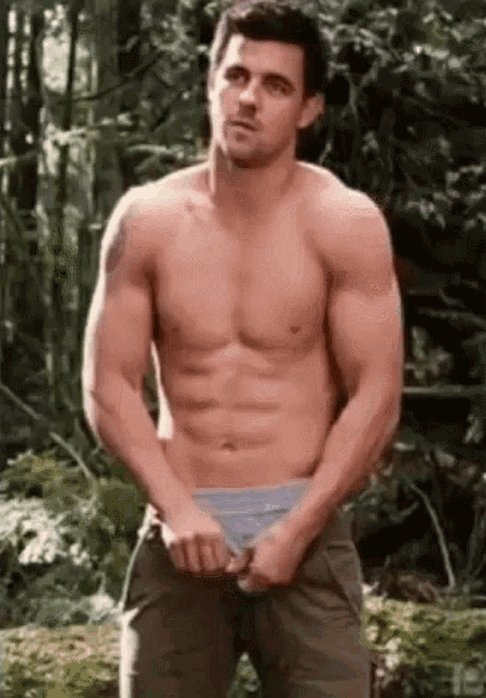 a shirtless man is standing in the woods taking his underwear off .