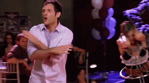 a man in a pink shirt is dancing in a room with balloons .