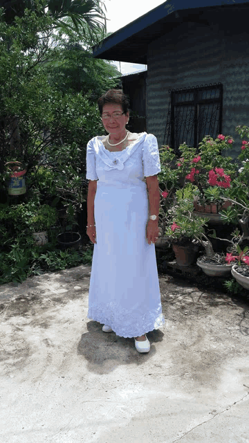 a woman in a long white dress stands in front of a house
