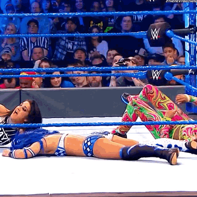 a woman laying on the ground in a wrestling ring with a w logo on the back of her shirt