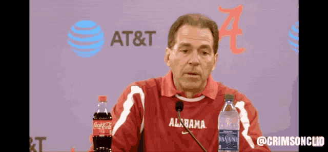 a man wearing an alabama shirt stands in front of a at & t logo