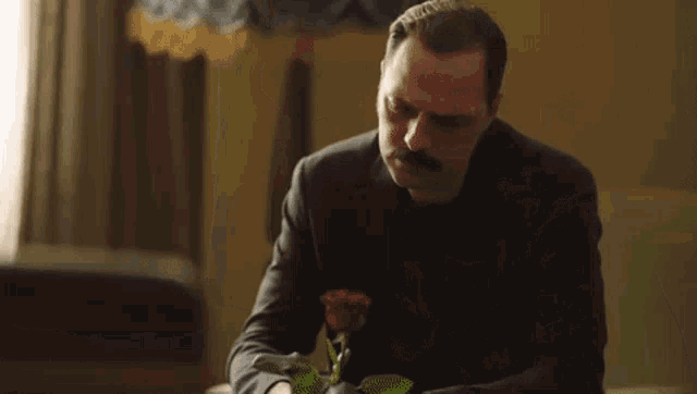 a man with a mustache is holding a red rose in his hands .
