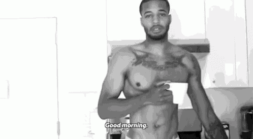 a shirtless man is standing in a kitchen holding a cup and saying `` good morning '' .