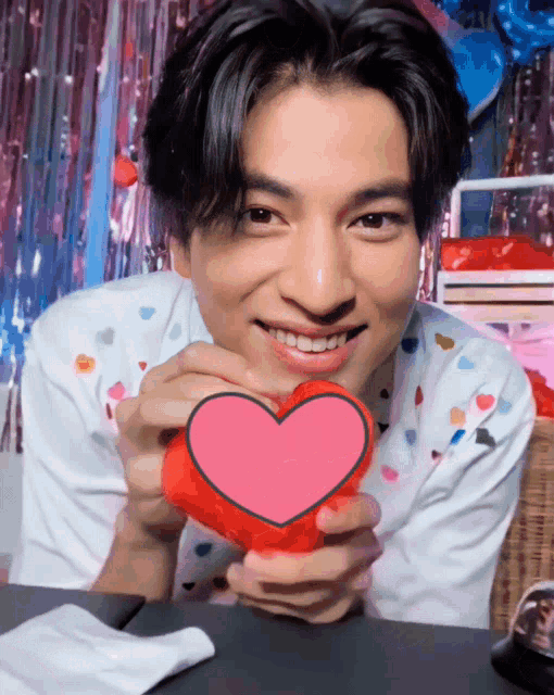 a man is holding a red heart in his hands and smiling