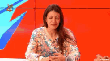 a woman in a sequined top is sitting in front of a screen that says los