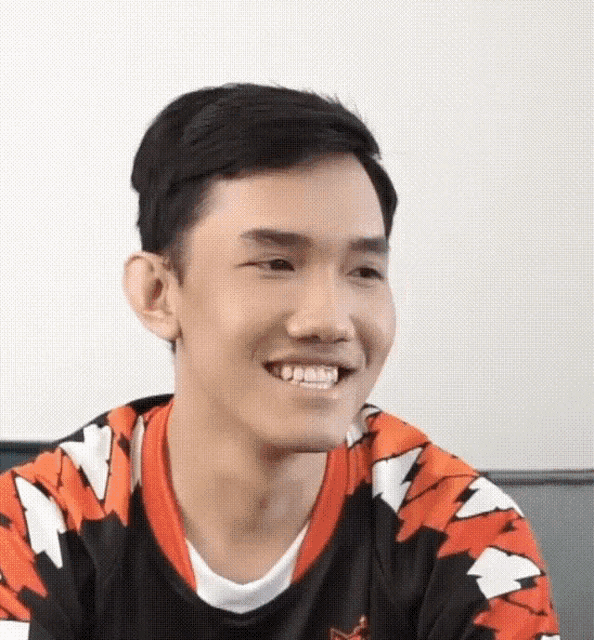 a young man wearing a black and orange shirt is smiling and looking at the camera .