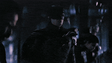 a man in a suit stands on a balcony overlooking a bridge at night