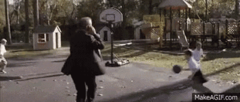 a man in a suit is talking on a cell phone while playing basketball with two children .