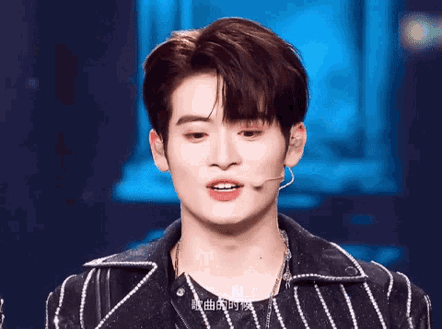 a close up of a young man wearing a microphone and a striped jacket