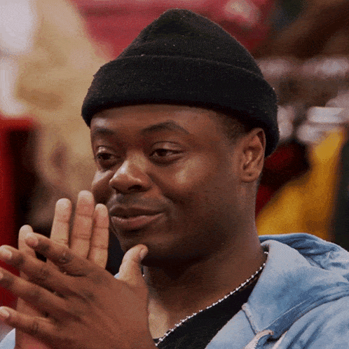 a man wearing a black beanie and a blue shirt is clapping his hands