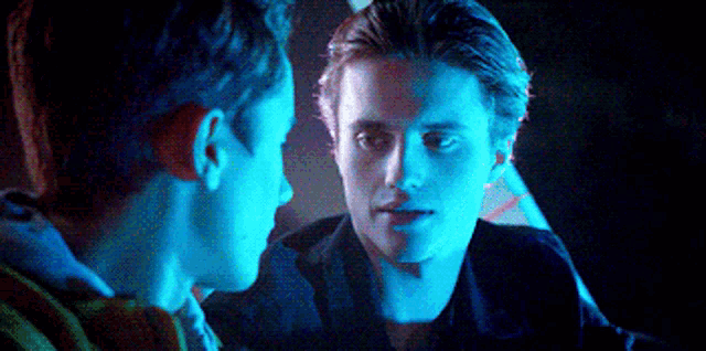 two men are looking at each other in a dark room with blue lights behind them