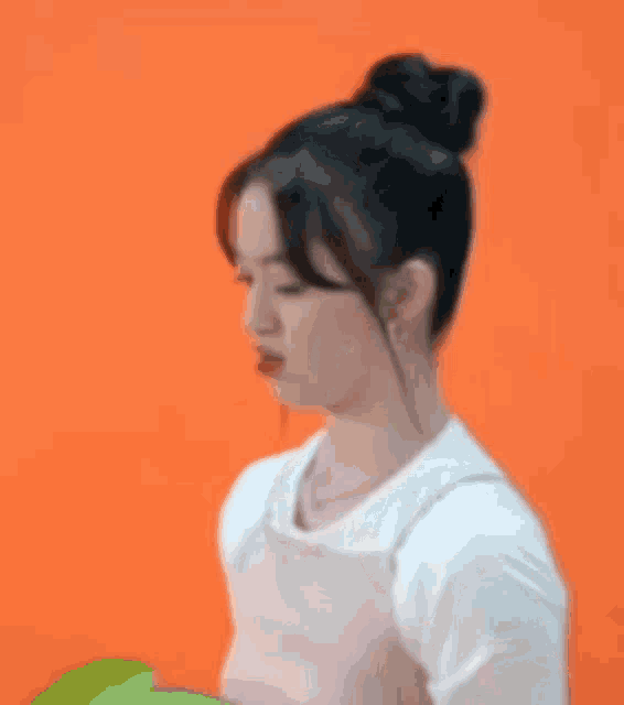 a woman in a pink apron is standing in front of an orange background and making a funny face .