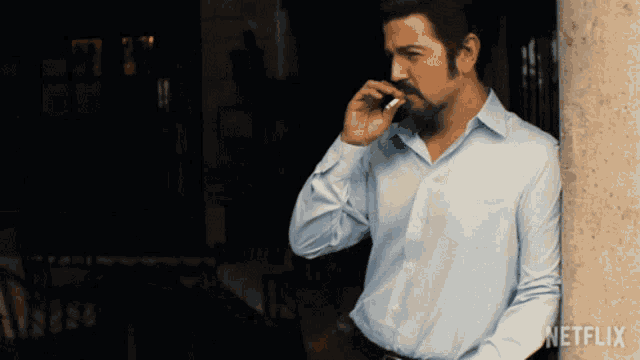 a man leaning against a wall smoking a cigarette with a netflix logo behind him