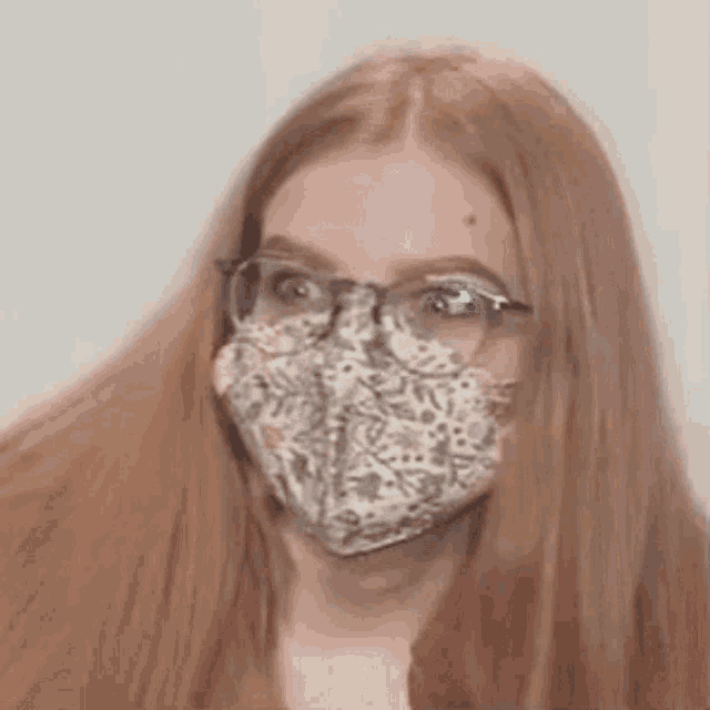 a woman with long red hair and glasses is wearing a mask .