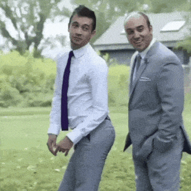 two men in suits are standing next to each other on a grassy field .