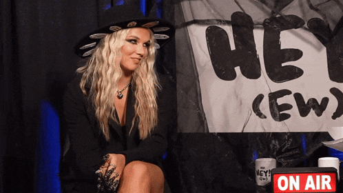 a woman is sitting in front of a sign that says hey crew