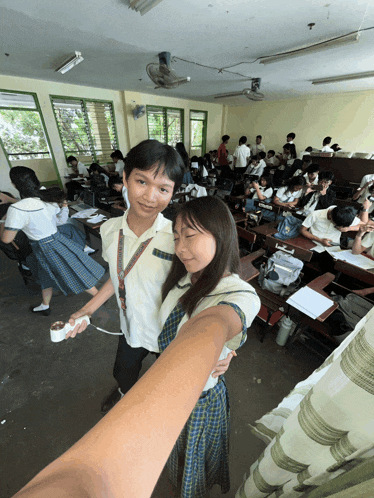 a boy and a girl are posing for a selfie in a classroom