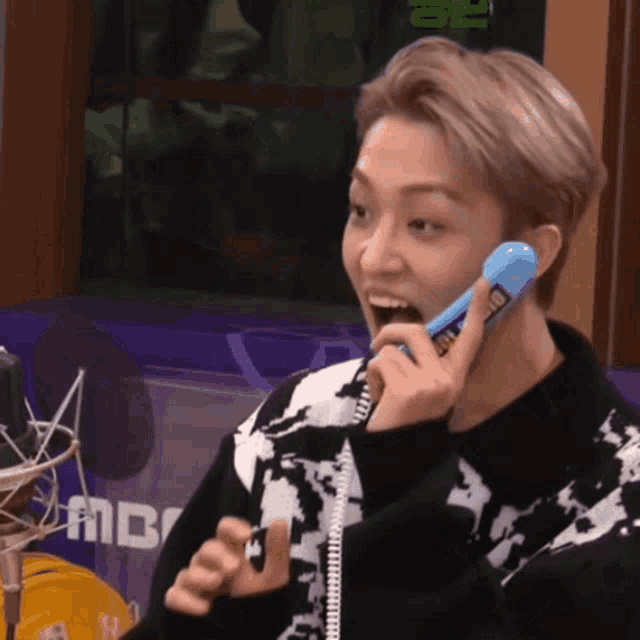 a young man is talking on a blue phone with a microphone in the background .