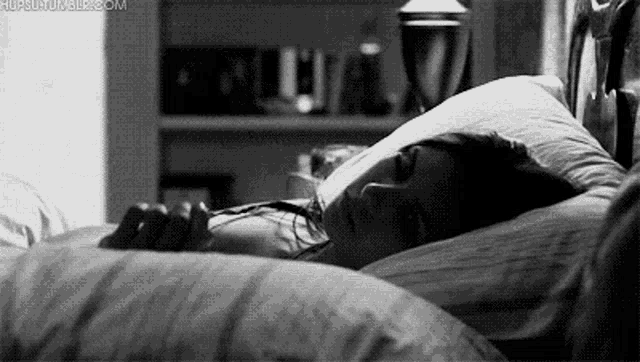 a black and white photo of a woman sleeping in a bed with a pillow .