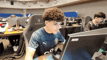 a man with curly hair is sitting in front of a computer wearing a blackrite chair