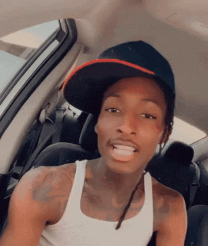 a man wearing a hat and a white tank top is sitting in the back seat of a car .
