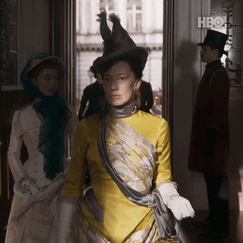 a woman in a yellow dress is standing in a doorway with a hbo logo in the background