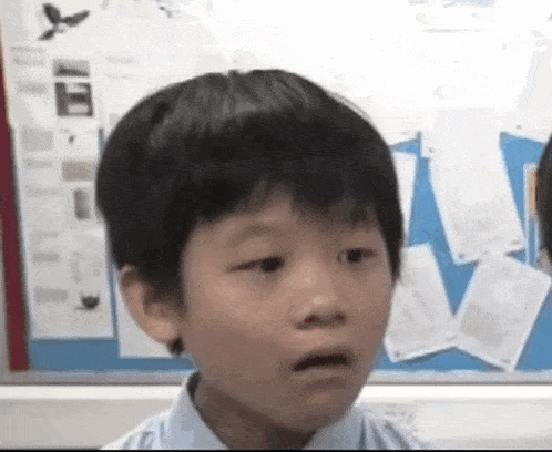 a young boy is making a funny face in front of a blue board in a classroom .