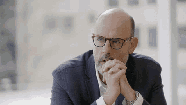 a bald man wearing glasses and a suit looks at something