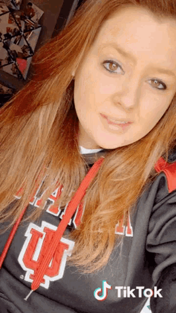 a woman wearing a sweatshirt with the letter u on it takes a selfie .