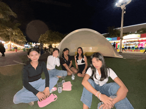 a group of girls are sitting on the grass in front of a large dome