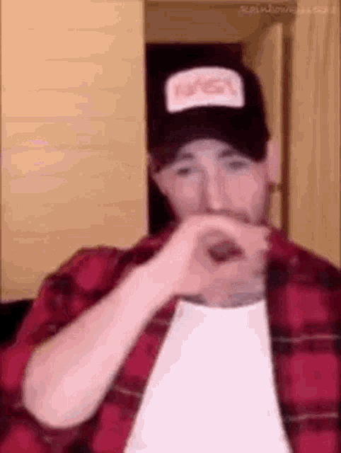 a man wearing a plaid shirt and a hat is making a heart shape with his hands .